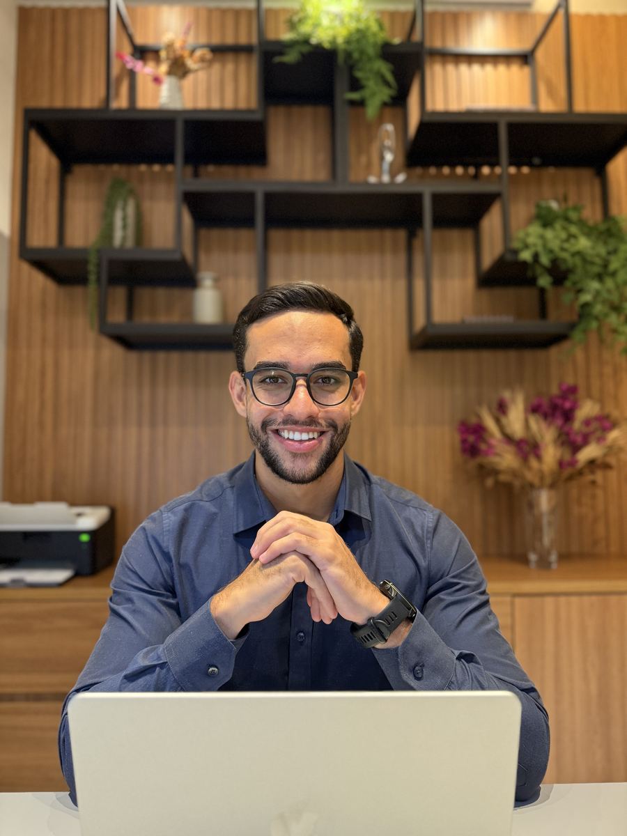 João Soares, fisioterapeuta, sorrindo à mesa do consultório