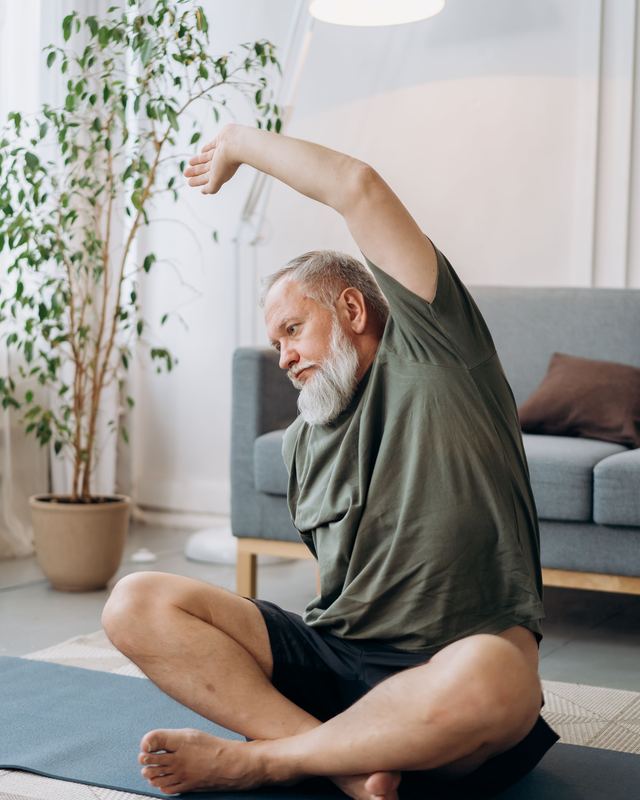 Homem de cabelo grisalho se alongando em casa